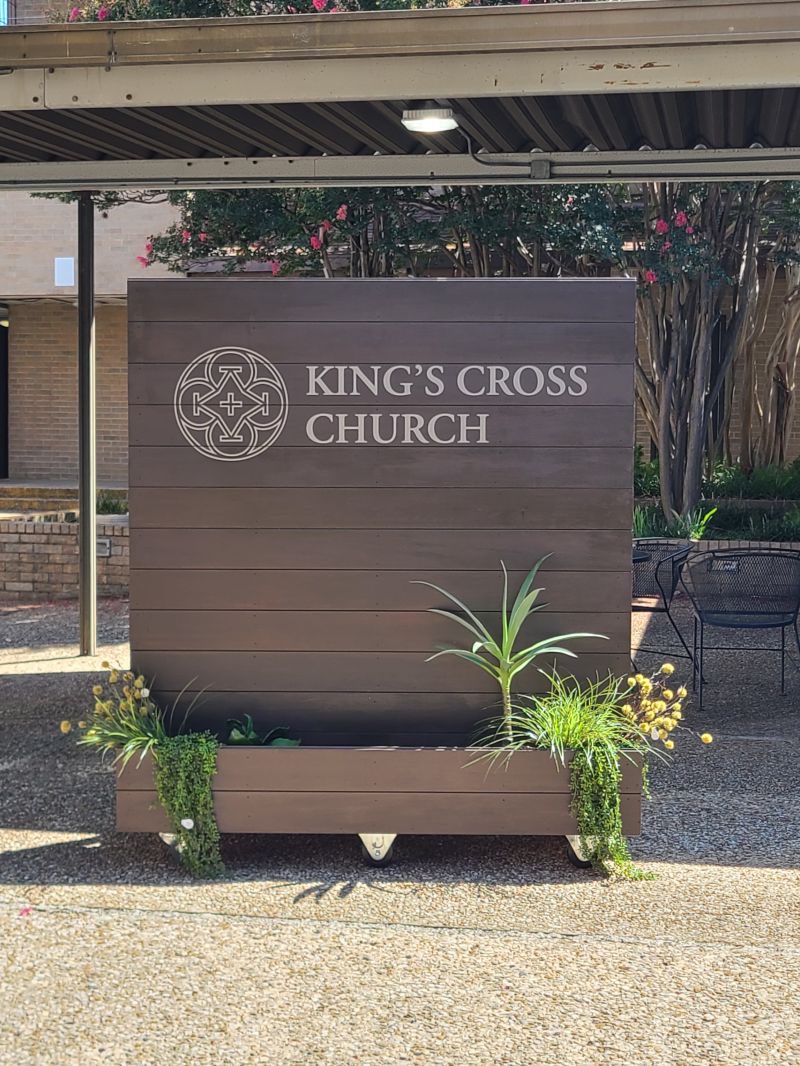 Freestanding branded entry sign with a planter base.